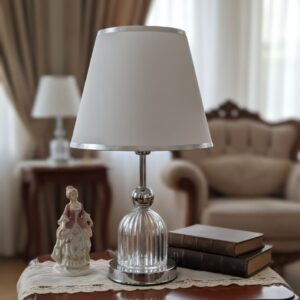 Lámpara de mesa de cristal y metal plateado con una pantalla blanca.