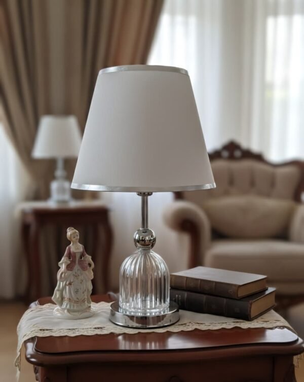 Lámpara de mesa de cristal y metal plateado con una pantalla blanca.