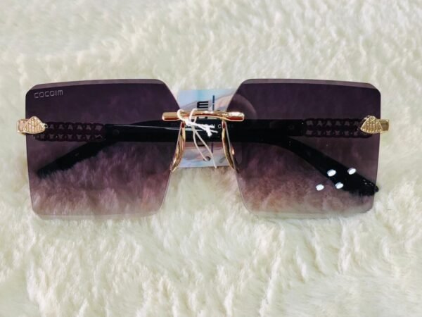 Gafas de sol con diseño cuadrado sin montura, detalles metálicos dorados en las patillas y lentes con degradado.