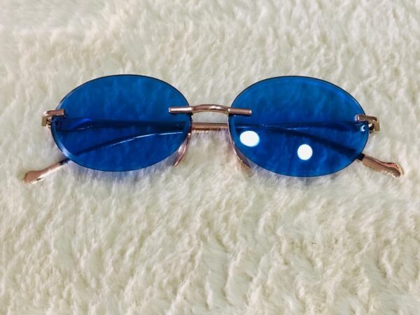 Gafas de sol de estilo "Morpheus" con lentes ovaladas azules sin montura y una estructura metálica dorada.