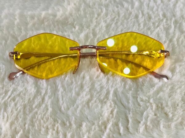 Gafas de sol con diseño hexagonal sin montura y lentes tintadas de color amarillo.